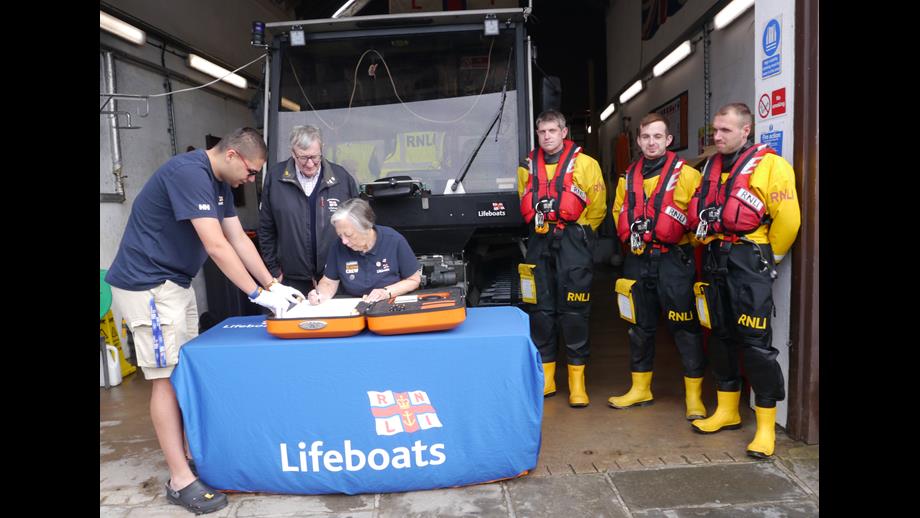 Roberta Duncan in front of the lifeboat tractor signing the 200th anniversary scroll with 3 members of the crew stood beside her