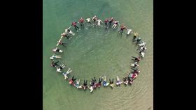Representatives from various agencies wearing PPE float in a circle joining hands in an image captured from above