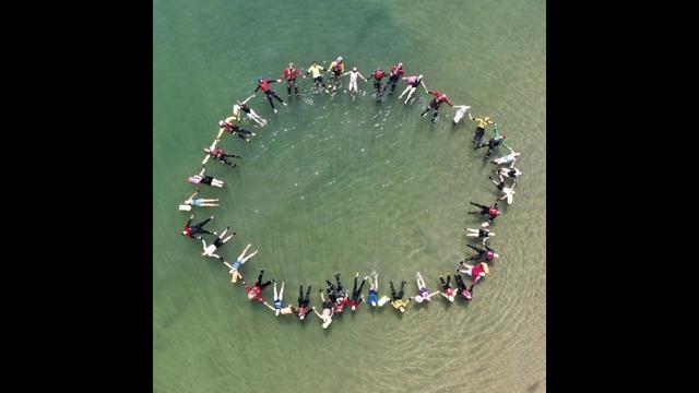 Representatives from various agencies wearing PPE float in a circle joining hands in an image captured from above
