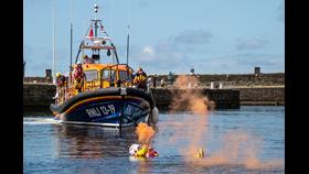 Lifeboat in harbour with crew member in water holding orange flare