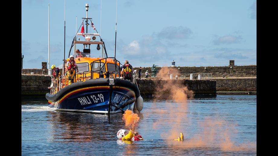 Lifeboat in harbour with crew member in water holding orange flare