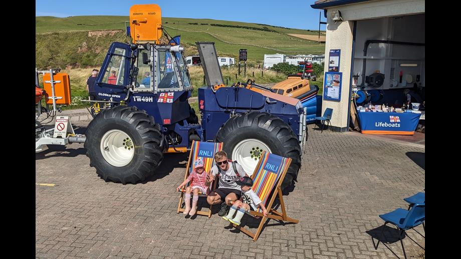 A father and his two young children take a rest in the large RNLI deckchairs beside the RNLI tractor