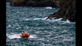 The small orange D-Class lifeboat in white capped seas with rugged cliffs in the background.

