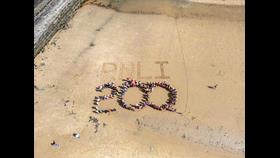 RNLI drawn in sand on the beach, with swimmers gathering over the numbers '200'
