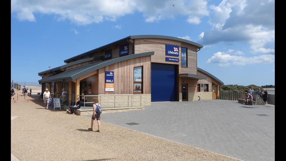 Boathouse with people walking past and blue sky