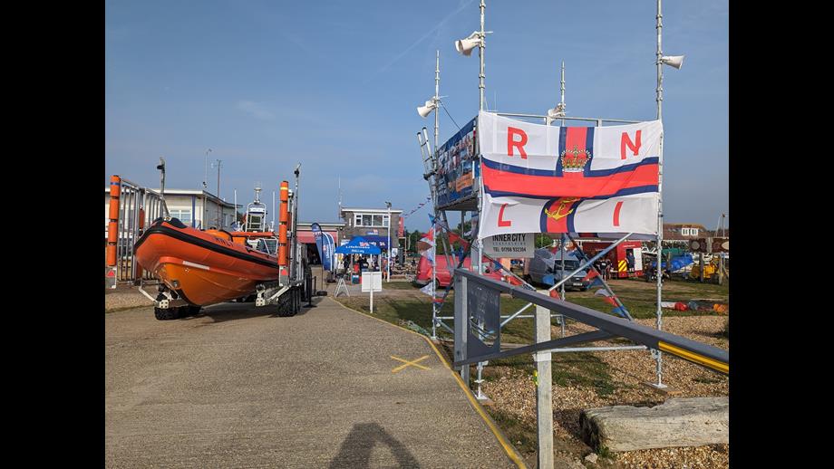 An inshore lifeboat and colourful RNLI flag in the foreground with the lifeboat station and boathouse behind