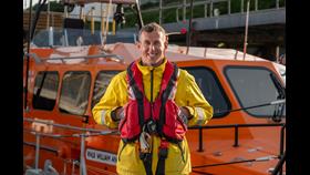 Photo of David Murray in his RNLI protective clothing standing in front of lifeboat