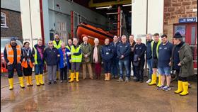 Cheque presentation with crew standing in front of boathouse