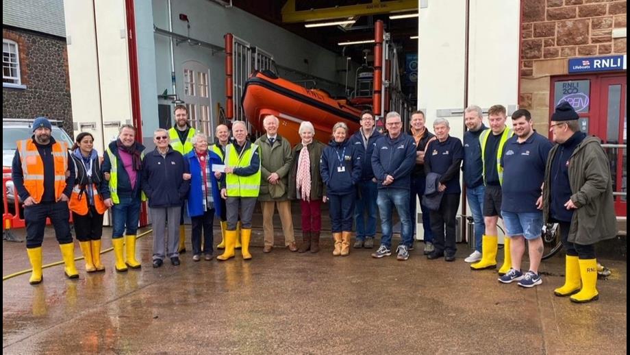Cheque presentation with crew standing in front of boathouse