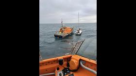 Shows two lifeboats at work on a yacht rescue