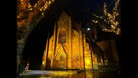 Front of cathedral lit in yellow light, seen between two tress.