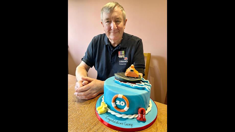 George with his celebration cake which has a lifeboat on the top, yellow wellies, life jacket and blue icing to represent the sea