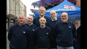 six men standing in front of a blue gazebo with RNLI printed on it