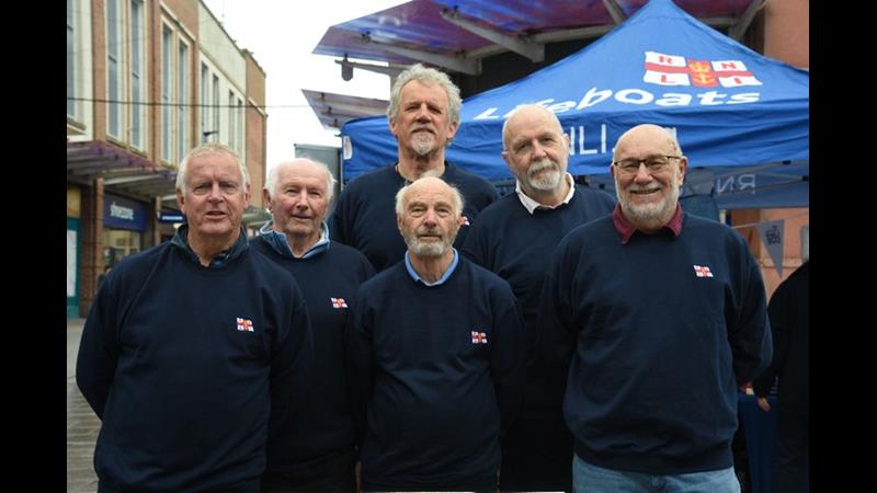 six men standing in front of a blue gazebo with RNLI printed on it