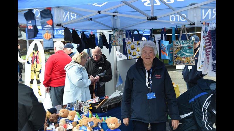 Woman in blue fleece behind a stall with people milling in background