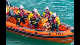 View from clifftop of lifeboat with crew holding wreath