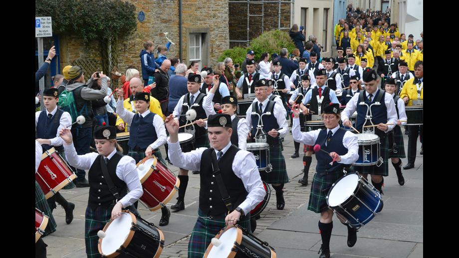 A section of drummers passing with crew behind in yellow