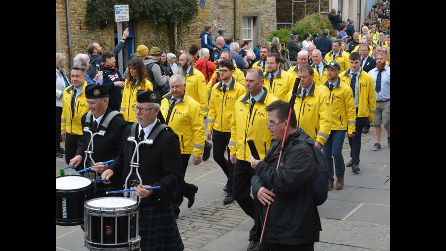 Stromness Lifeboat Volunteer crew (in yellow) marching with the band