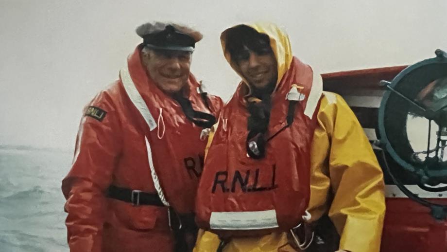 Close-up of two men on boat at sea wearing old life jackets and RNLI coats