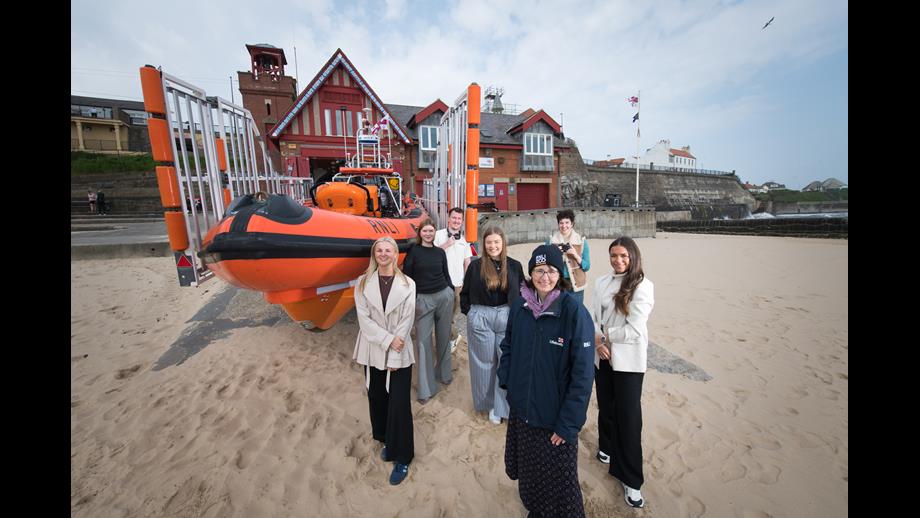 6 students and RNLI woman, infront of B-Class Lifeboat on sand outside of Cullercoats Lifeboat Station