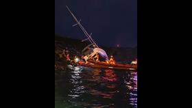 The stricken yacht lies across rocks in the background and the RNLI inshore lifeboats are in the foreground. It is dark, but the sea is calm.