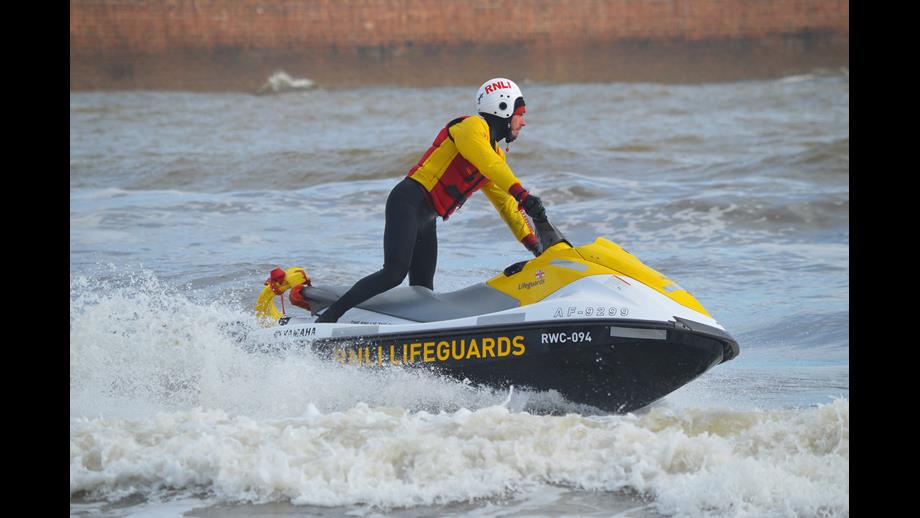 Male lifeguard on yellow jet ski wear wetsuit, lifejacket and helmet