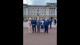 Five representatives stand-in in line with Buckingham Palace behind. 