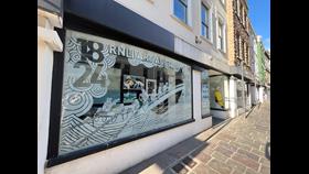 The decorated window display showing an etched outline of an Atlantic 85 perging into an old rowing lifeboat with the 1824 date and the words &quot;RNLI Art Auction&quot;. The paintings for auction are behind the etched window.