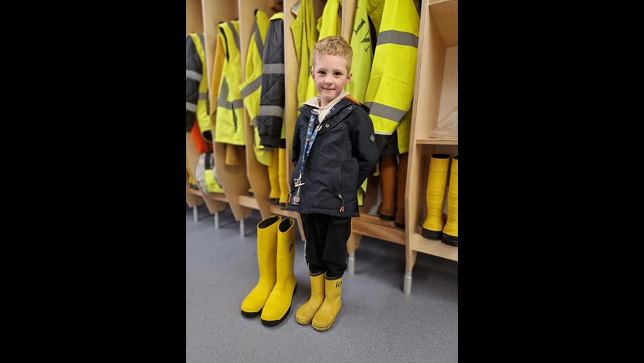 6 year old William Stockley in yellow wellies standing next to a large pair of crew RNLI wellies