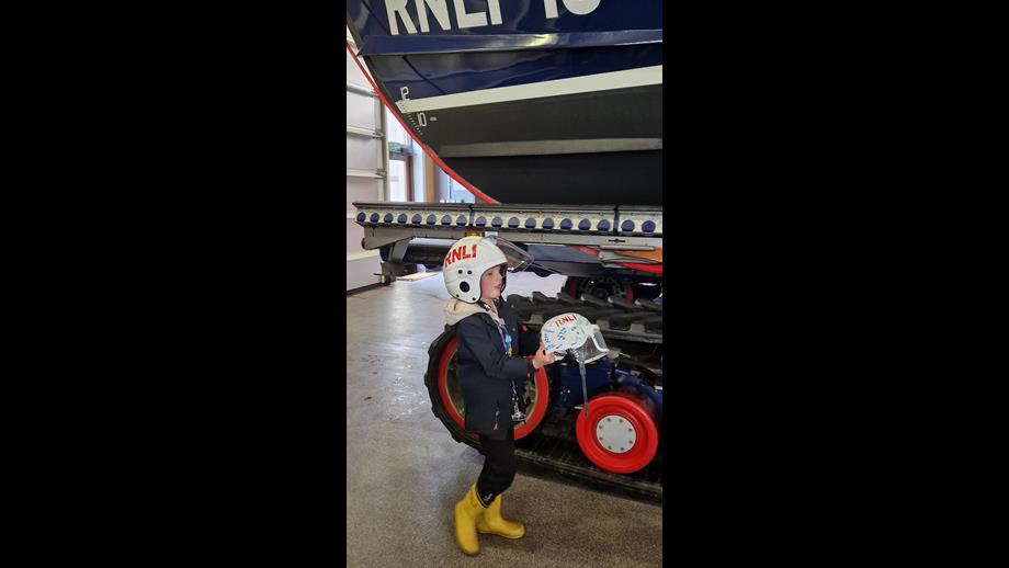 Young lad holding RNLI crew helmet and wearing another
