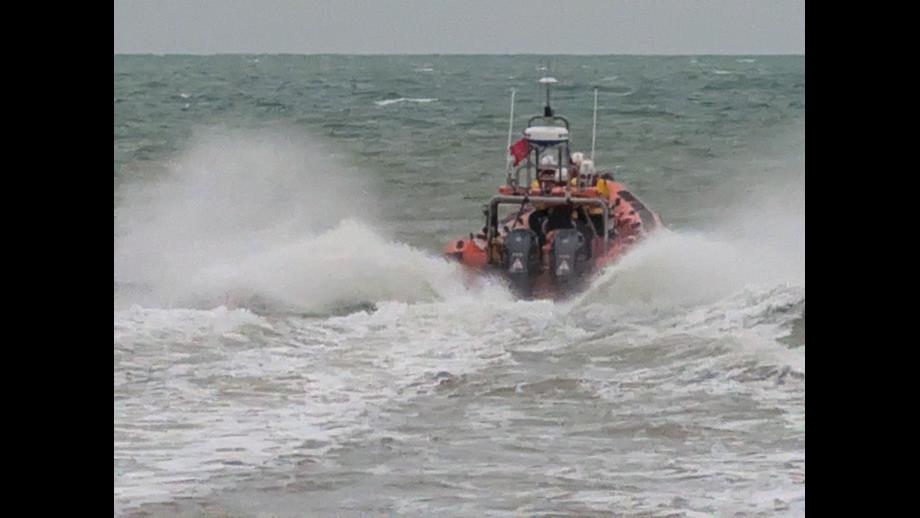 An orange RNLI lifeboat, the Jean McIvor from Littlestone , powers through the waves creating spectacular surf