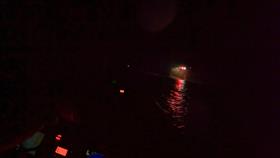 An image showing how dark it was, the lights of a helicopter can be seen in the image and reflections of the lights on the water, only illuminated parts of the lifeboat can be seen.