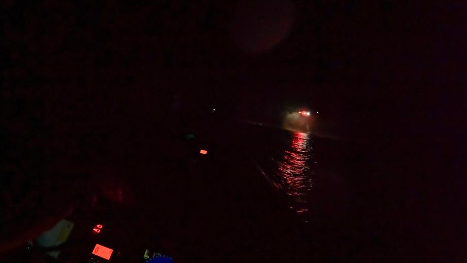 An image showing how dark it was, the lights of a helicopter can be seen in the image and reflections of the lights on the water, only illuminated parts of the lifeboat can be seen.