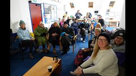 People in outdoor wear gather in front of a presenter at water safety talks