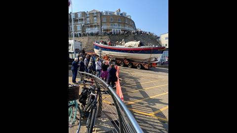 A line of people watching heritage lifeboat being driven away on a lorry.