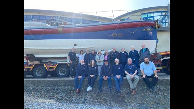 Long line of people in RNLI branded clothes alongside heritage lifeboat.