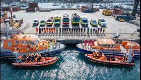 A gathering of Jersey's emergency services personnel on the harbour-front at St Helier, dramatically taken by drone. There are lifeboats in the foreground, personnel lined up on the dock edge and vehicles including ambulances, fire engines and police cars lined up behind. 