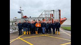 Crew standing in front of orange lifeboat holding orange scroll box 