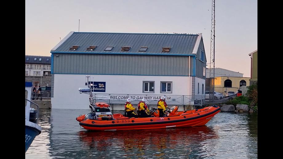 Four crew on board an Atlantic 85 lifeboat, on the water just after launching, with the Galway lifeboat station in the background.