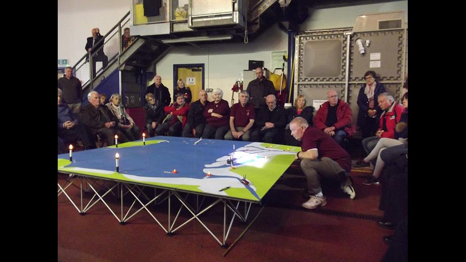 An audience sit round a table diorama of the Irish Sea with models