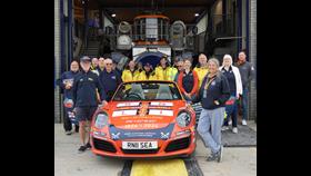 A group of people stand around an orange car