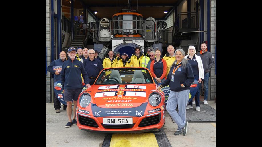 A group of people stand around an orange car