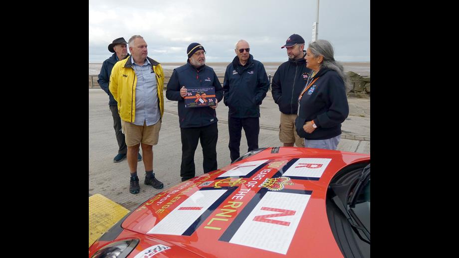 A group of peop[le stand around a car with an RNLI flag on the bonnet