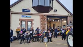 Group of musicians sitting outside station playing ukuleles 