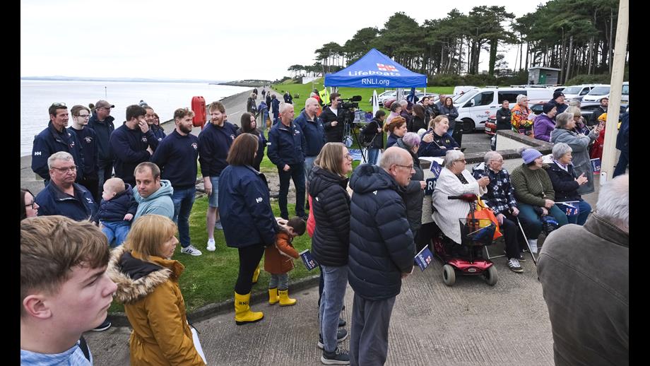 Large group of people gathered outside lifeboat station watching musicians 