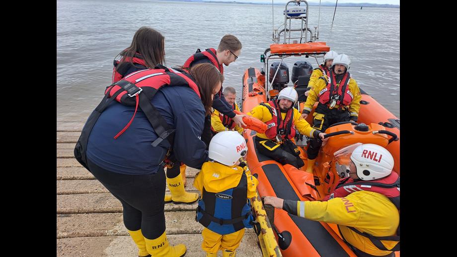 People standing on slipway handing over orange box to lifeboat crew in the boat