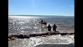 The lifeboat can be seen in the water with two shore crew members walking back to shore, wading through the water.