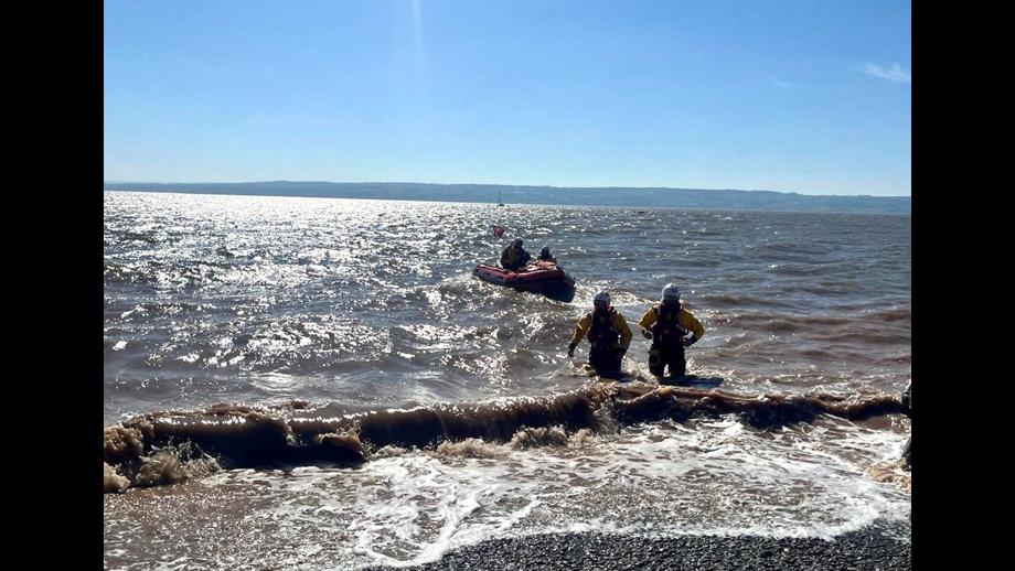 The lifeboat can be seen in the water with two shore crew members walking back to shore, wading through the water.
