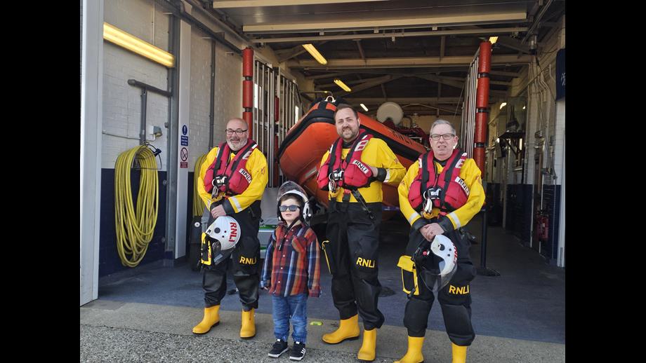 Seb standing with three crew members in lifeboat kit in front of the Atlantic 85