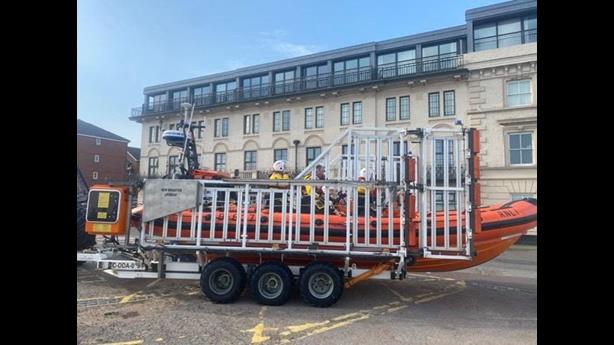 Full frame shot of the lifeboat, from the starboard side, sat in the carriage. Crew can be seen onboard, preparing the boat for service.